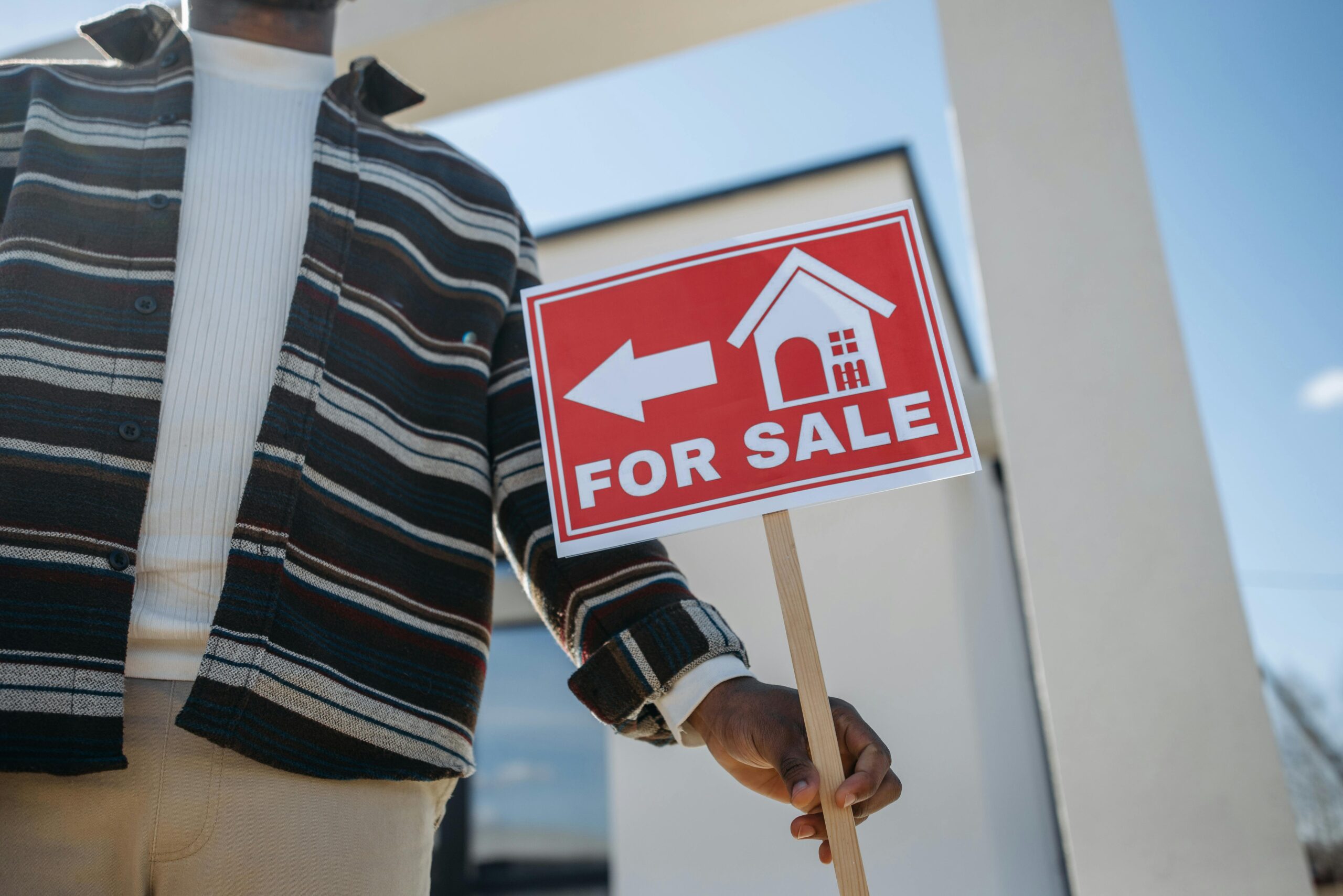 person in stripes long sleeves holding the for sale sign