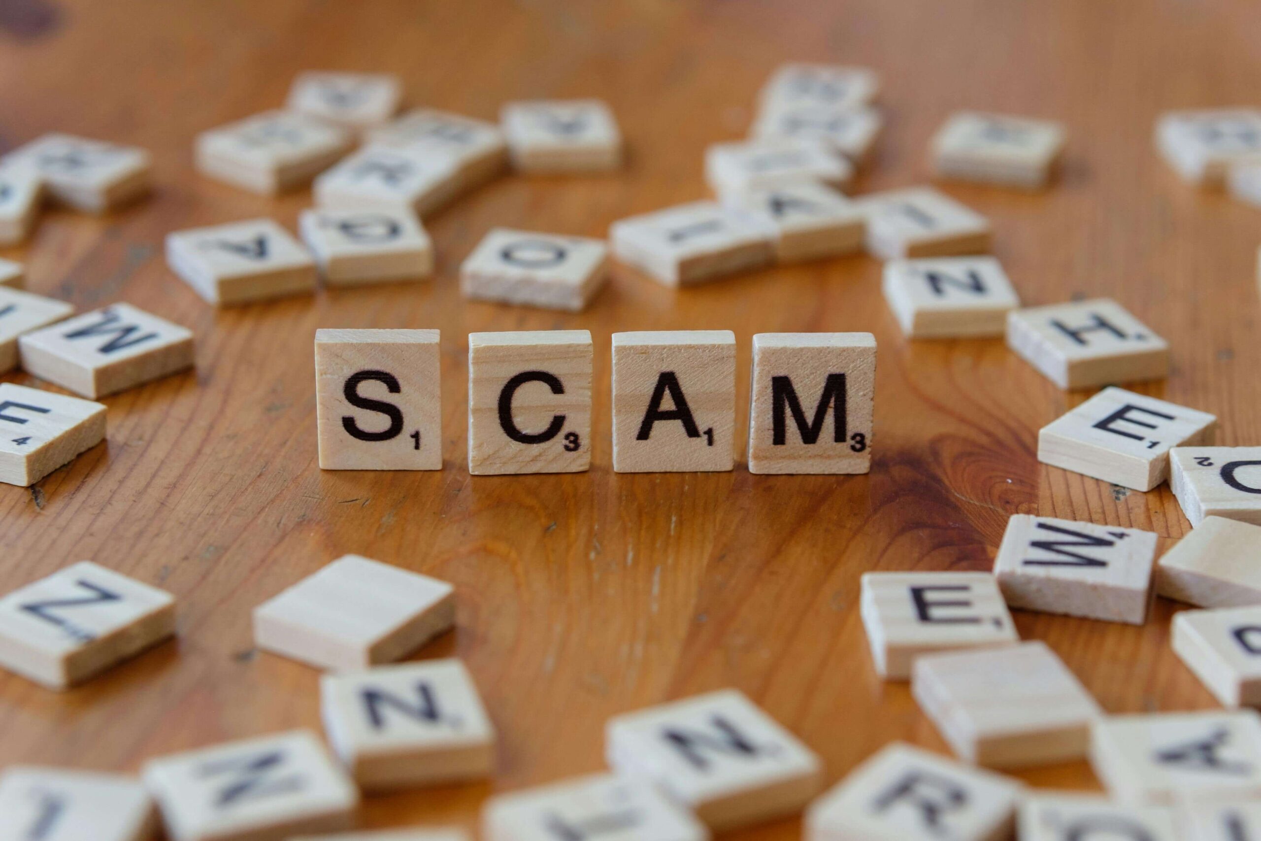 scrabble tiles spelling scam on wooden table